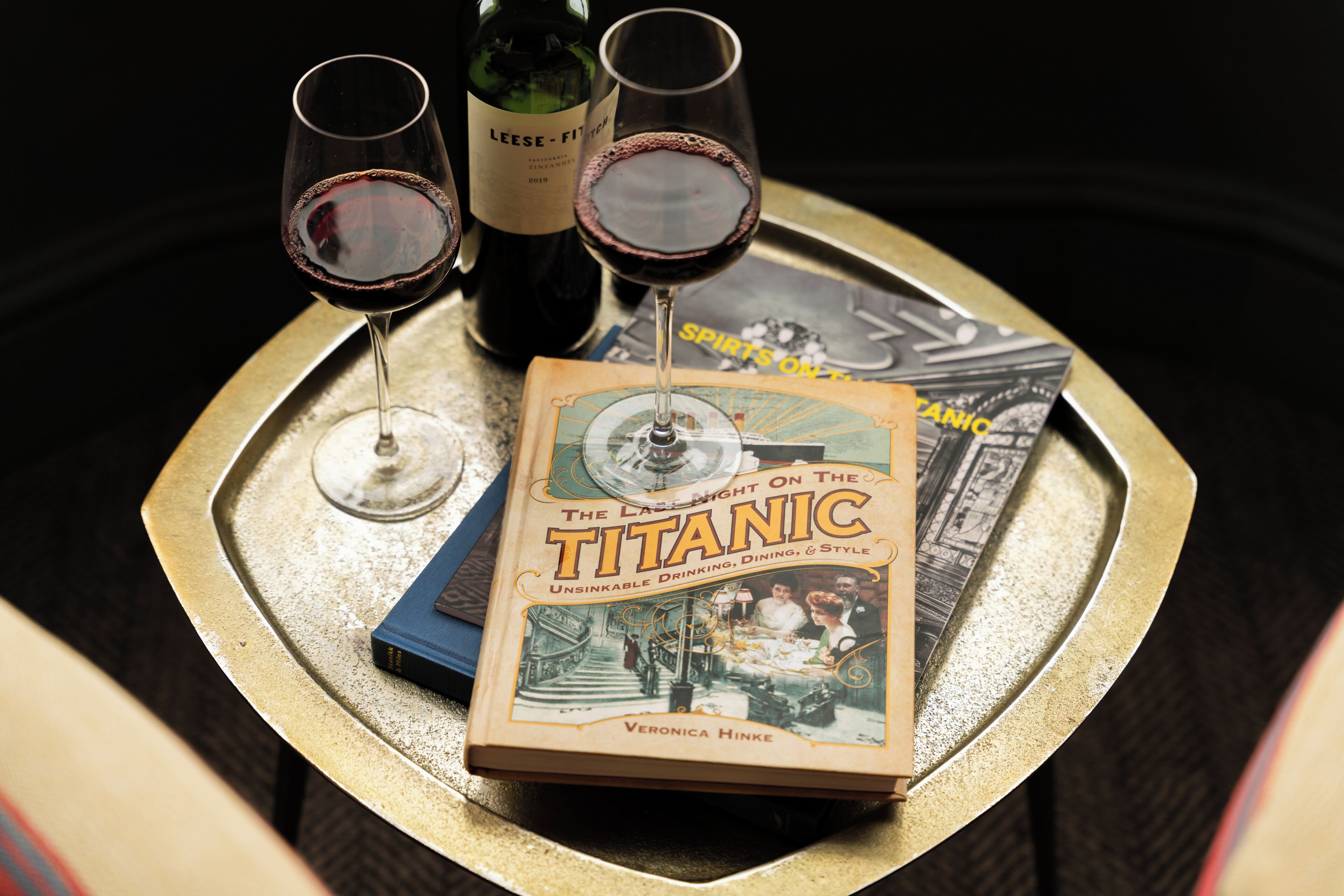 A tray with a book titled 'The Last Night on the Titanic' and two glasses of red wine.