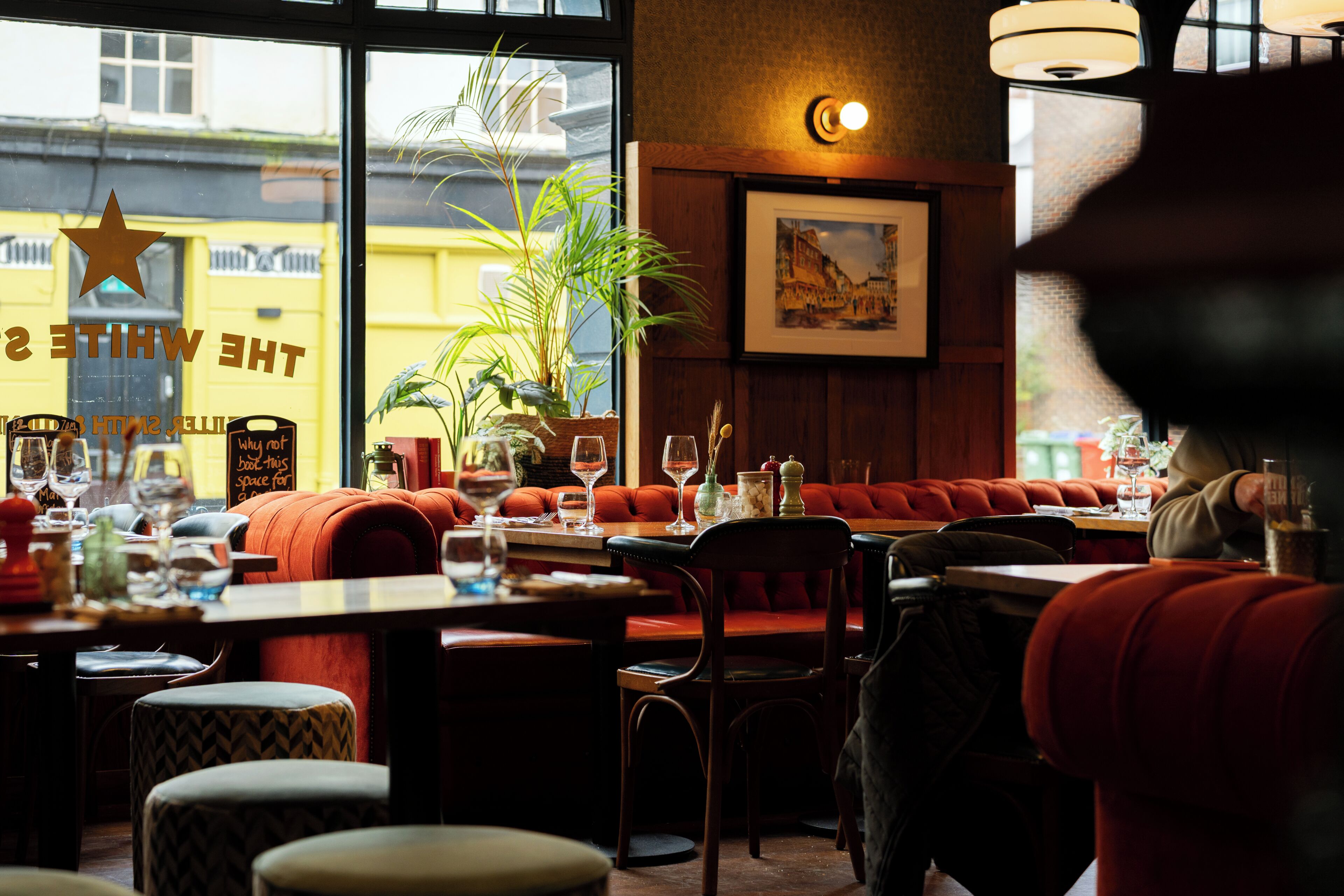 A restaurant interior with booths, tables, and a large window with a view of a yellow building.
