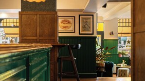 Una zona de bar con muebles de madera, carteles enmarcados en la pared y una silla tapizada en verde.
