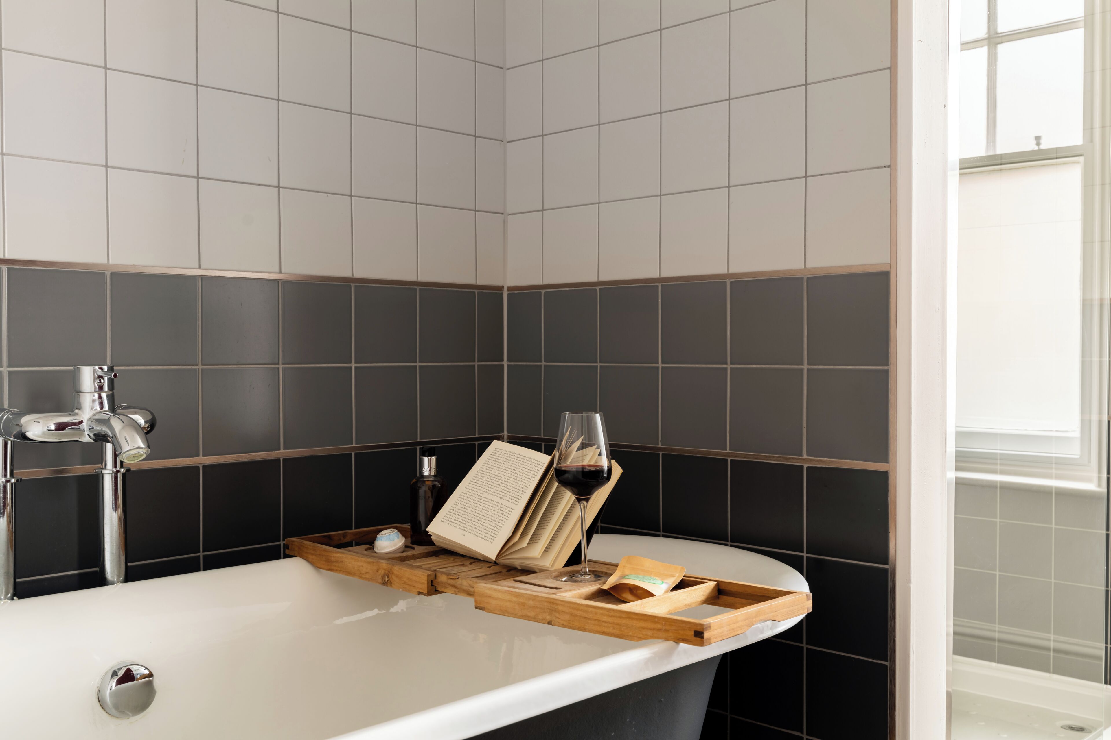 A bathroom with a bathtub, a book, a glass of wine, and a tray.