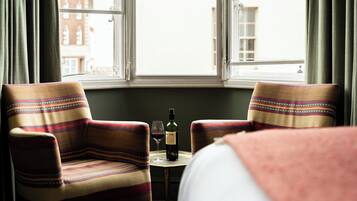 A room with two armchairs, a small table with a bottle and glass, and a bed with a blanket.