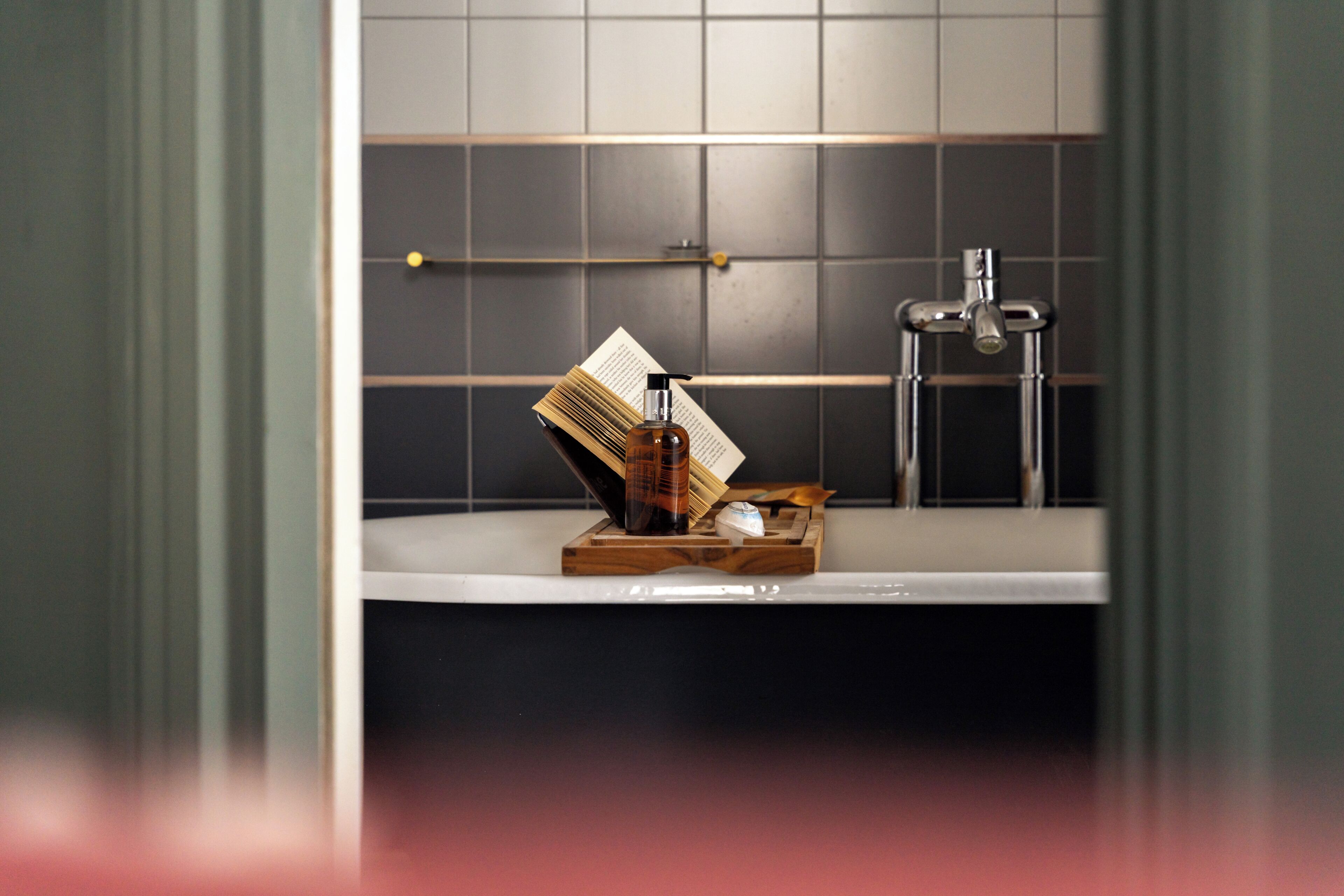 Un bagno con un piano d'appoggio bianco, un vassoio di legno con articoli da toilette, un libro e un rubinetto.