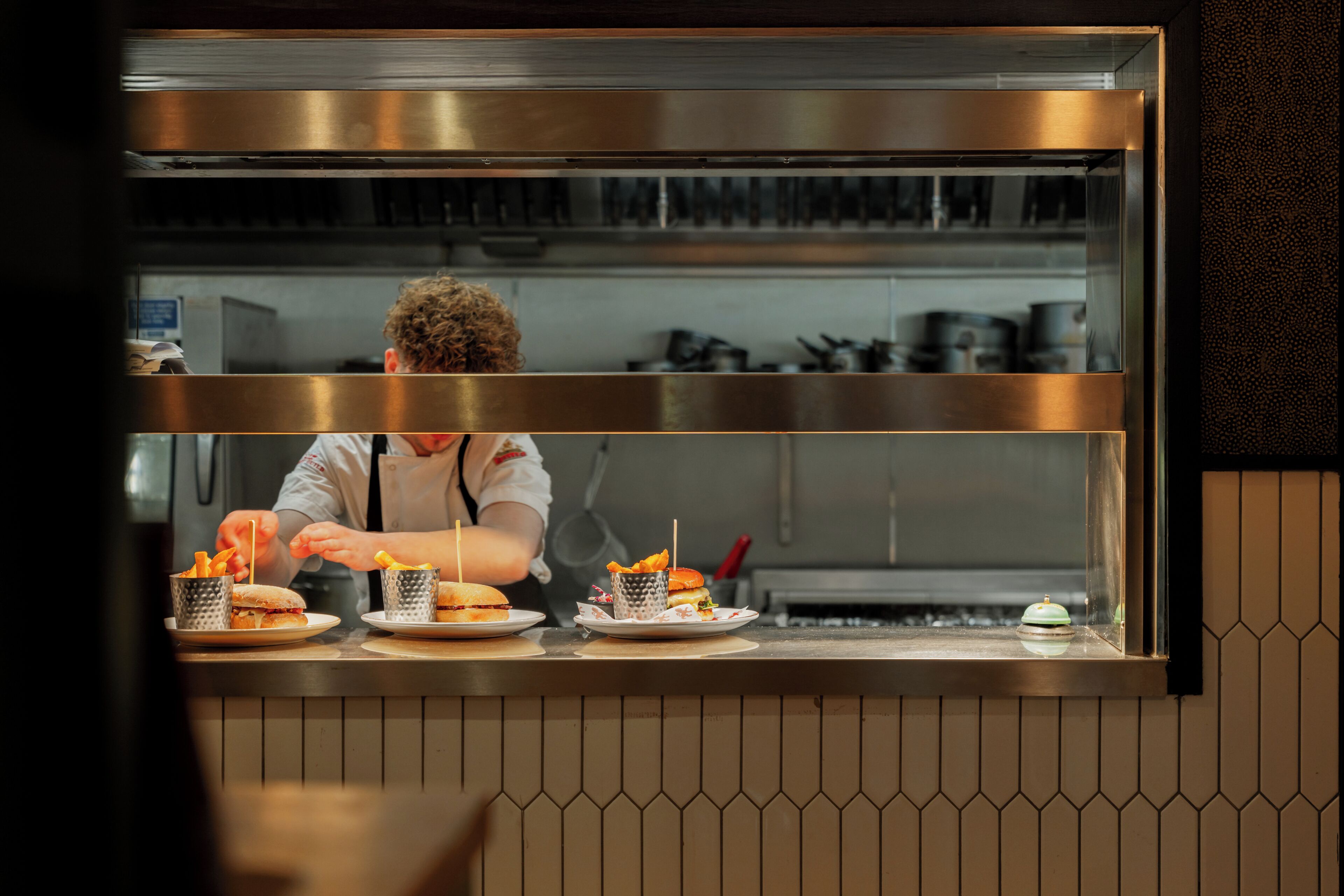 A kitchen counter with a chef preparing food, a stainless steel backsplash, and a tiled wall.