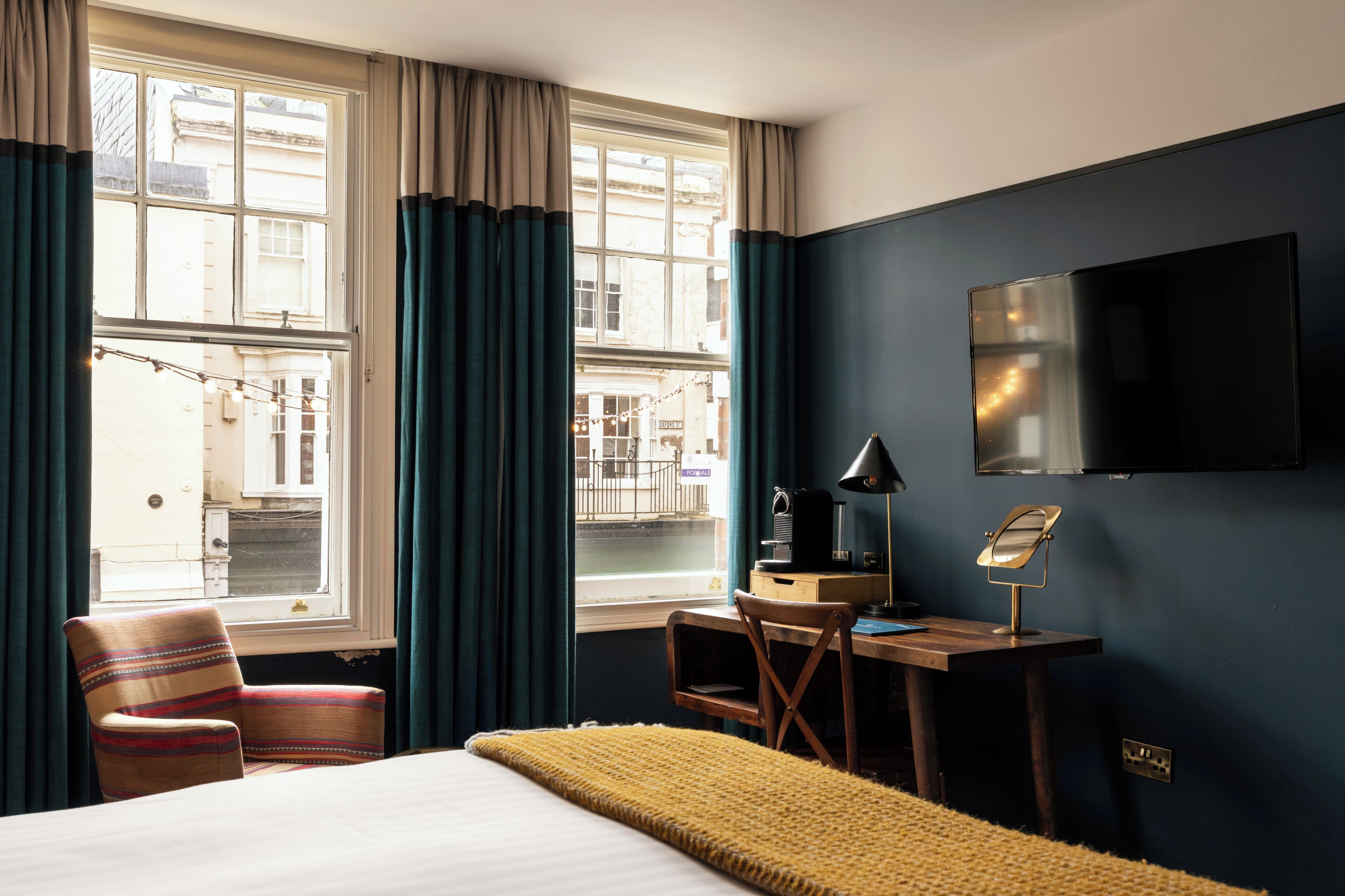A hotel room with a bed, a desk with a lamp, a chair, a TV, and a window with curtains.