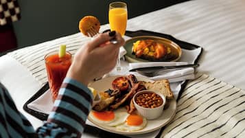 A breakfast tray with eggs, bacon, toast, beans, and a glass of orange juice on a bed.