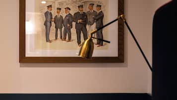 A framed picture of men in suits on a wall, a desk lamp, and a bed with a white headboard.