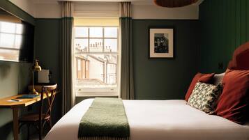 A bedroom with a bed, a desk, a chair, a window with curtains, and a framed picture on the wall.