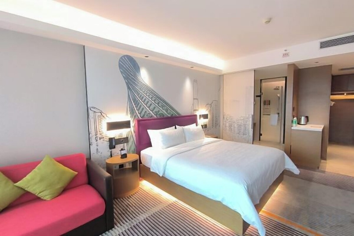 Habitación de hotel con una cama, un sofá rojo, una mesita de noche y una pared con un diseño original.