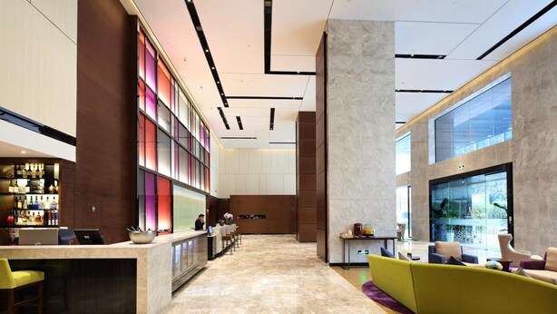 A modern lobby with a reception desk, bar area, seating, and a large window. - Hampton by Hilton Guangzhou Zhujiang New Town (Guangzhou)