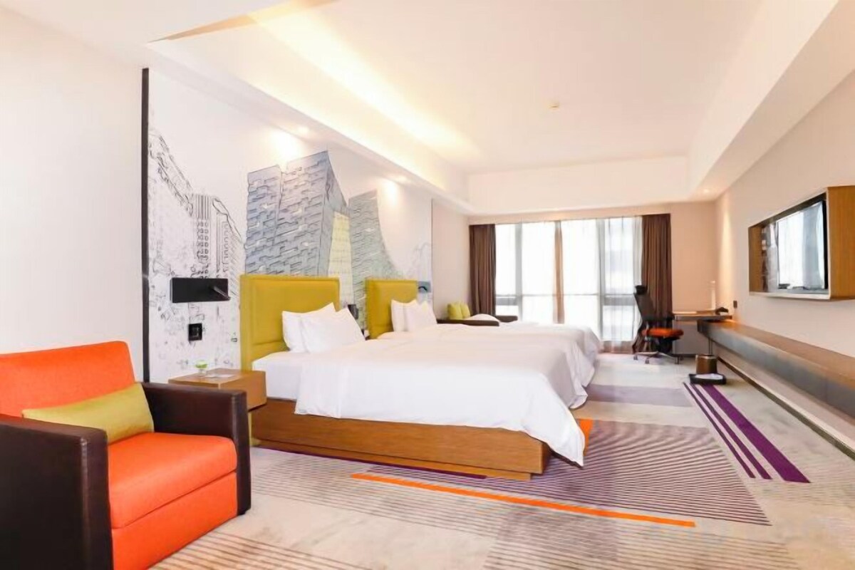 Habitación de hotel con una cama grande, dos mesitas de noche, un televisor y un rincón de estar con una silla.