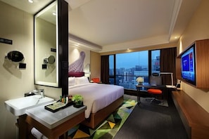 A hotel room with a bed, a desk, a TV, a large mirror, and a city view. - Hampton by Hilton Guangzhou Zhujiang New Town (Guangzhou)