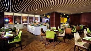 A restaurant with a modern interior, featuring a central bar area, multiple dining tables with chairs, and a wooden ceiling. - Hampton by Hilton Guangzhou Zhujiang New Town (Guangzhou)