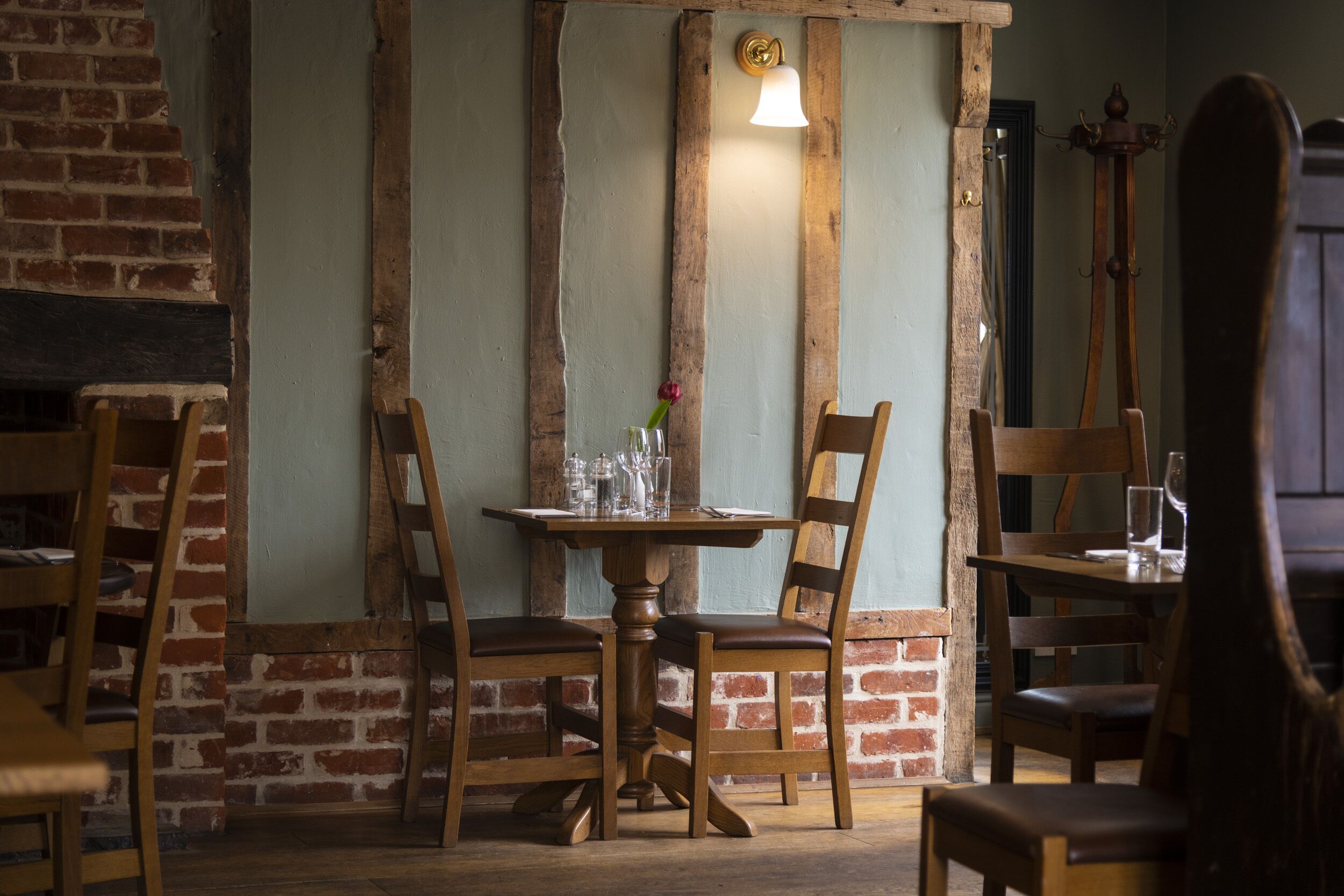 A rustic dining area with exposed brick walls, wooden chairs, a wooden table, and a hanging light fixture.
