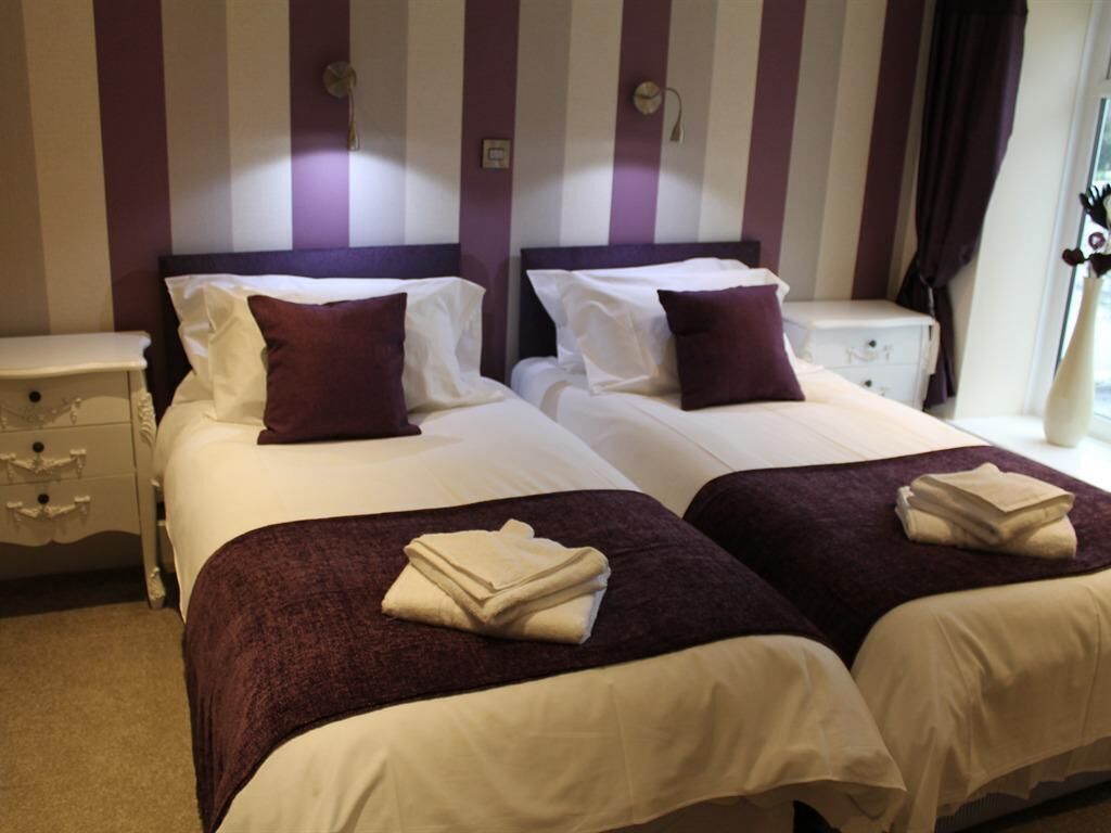 A hotel room with two beds, striped wallpaper, and a nightstand with drawers.