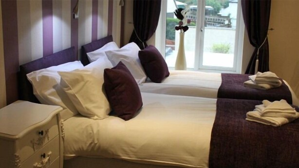 Una habitación de hotel con dos camas, una mesita de noche y un ventanal con cortinas.
