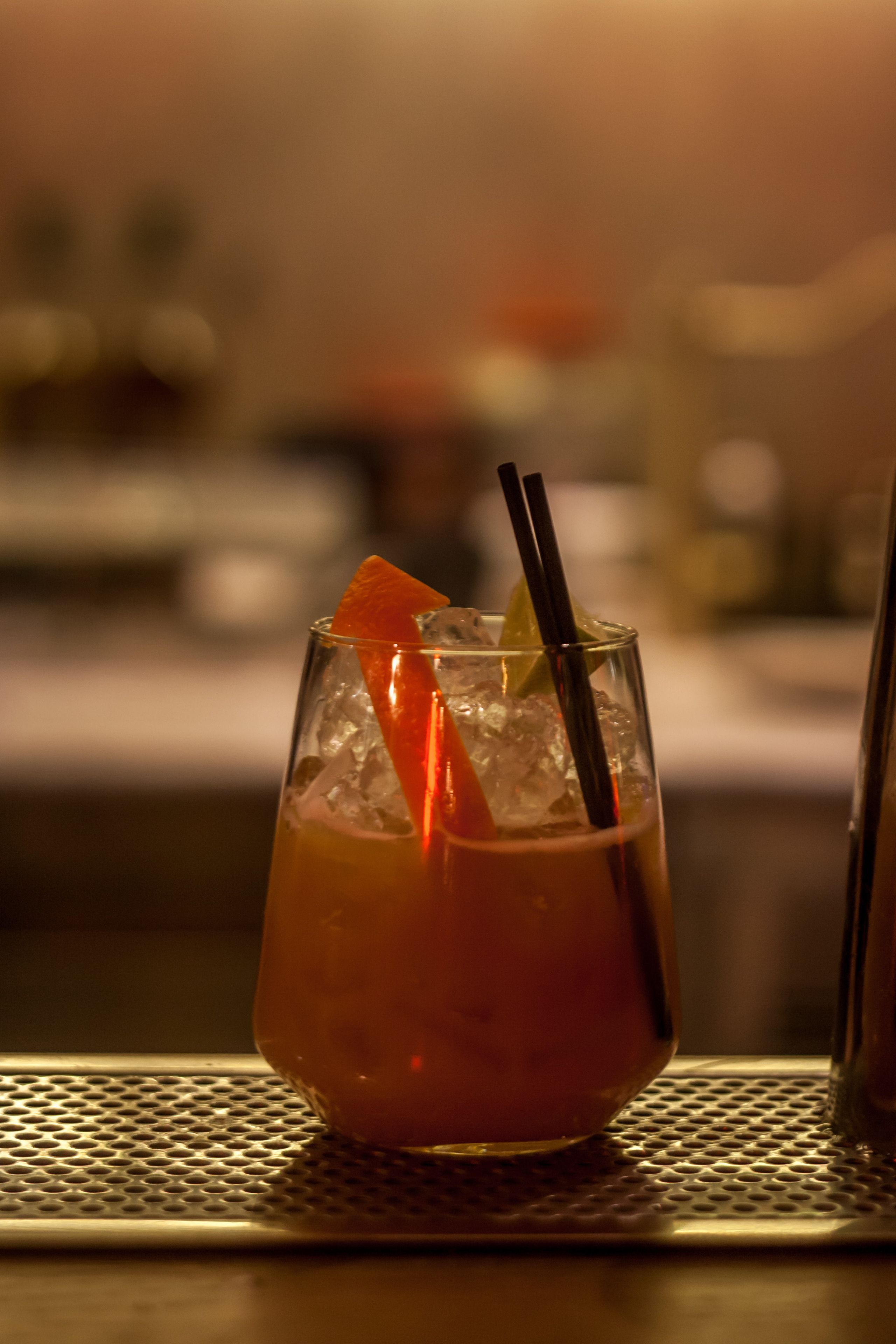 Ein Glas mit einem gekühlten Getränk, einer Limettenscheibe und zwei Strohhalmen auf einer Bar.