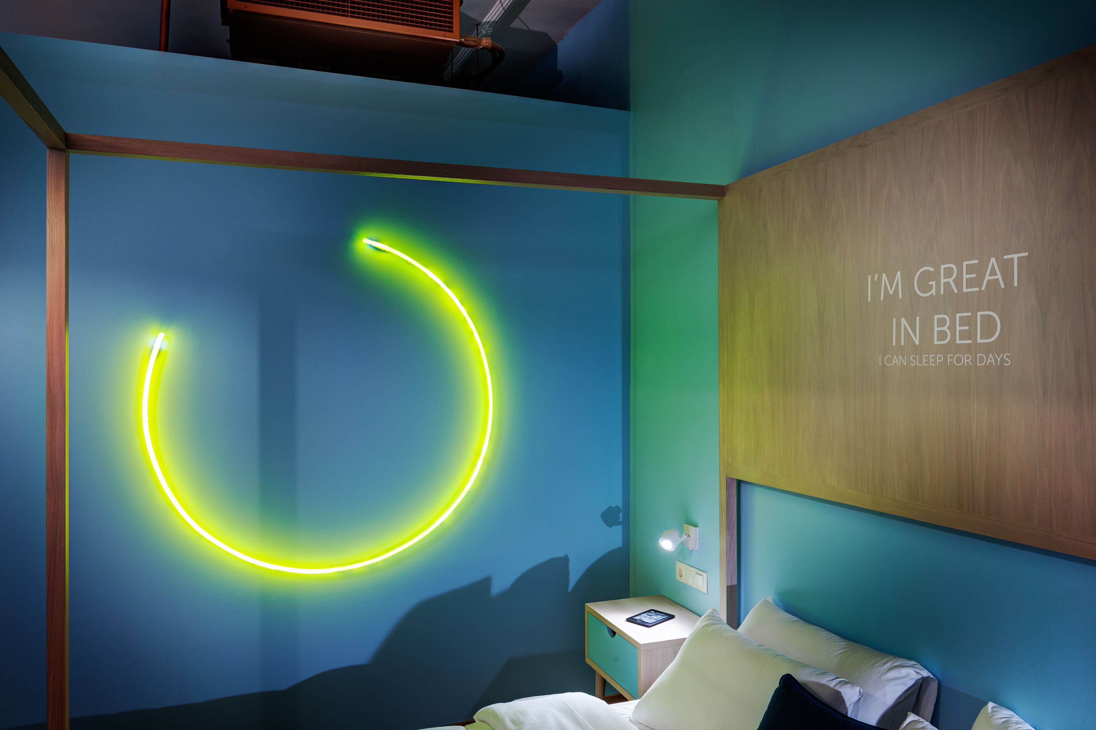 Quarto moderno com luz neon, mesa de cabeceira e parede com frase motivacional.