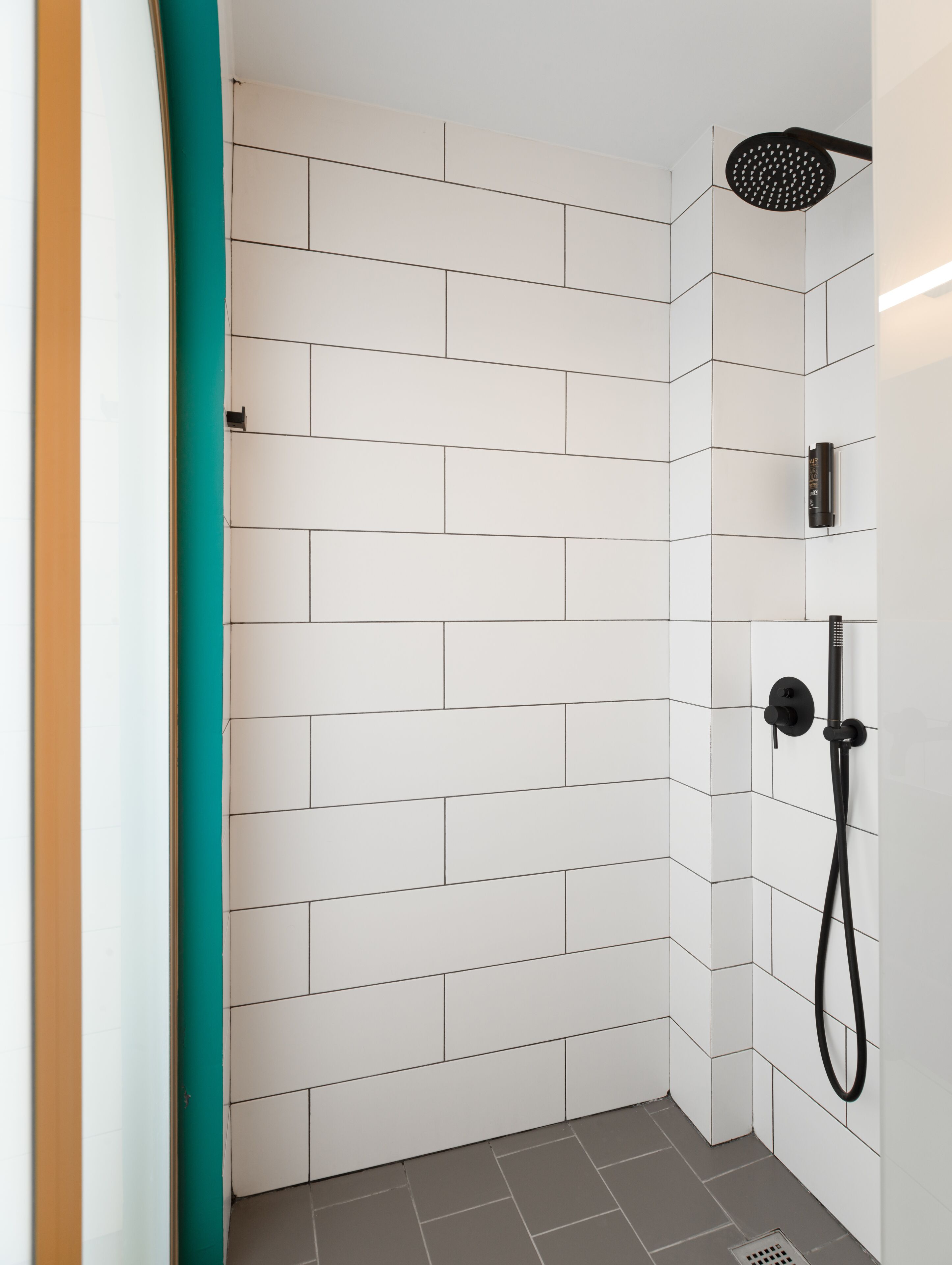 A modern shower area with white tiled walls and a black handheld showerhead.