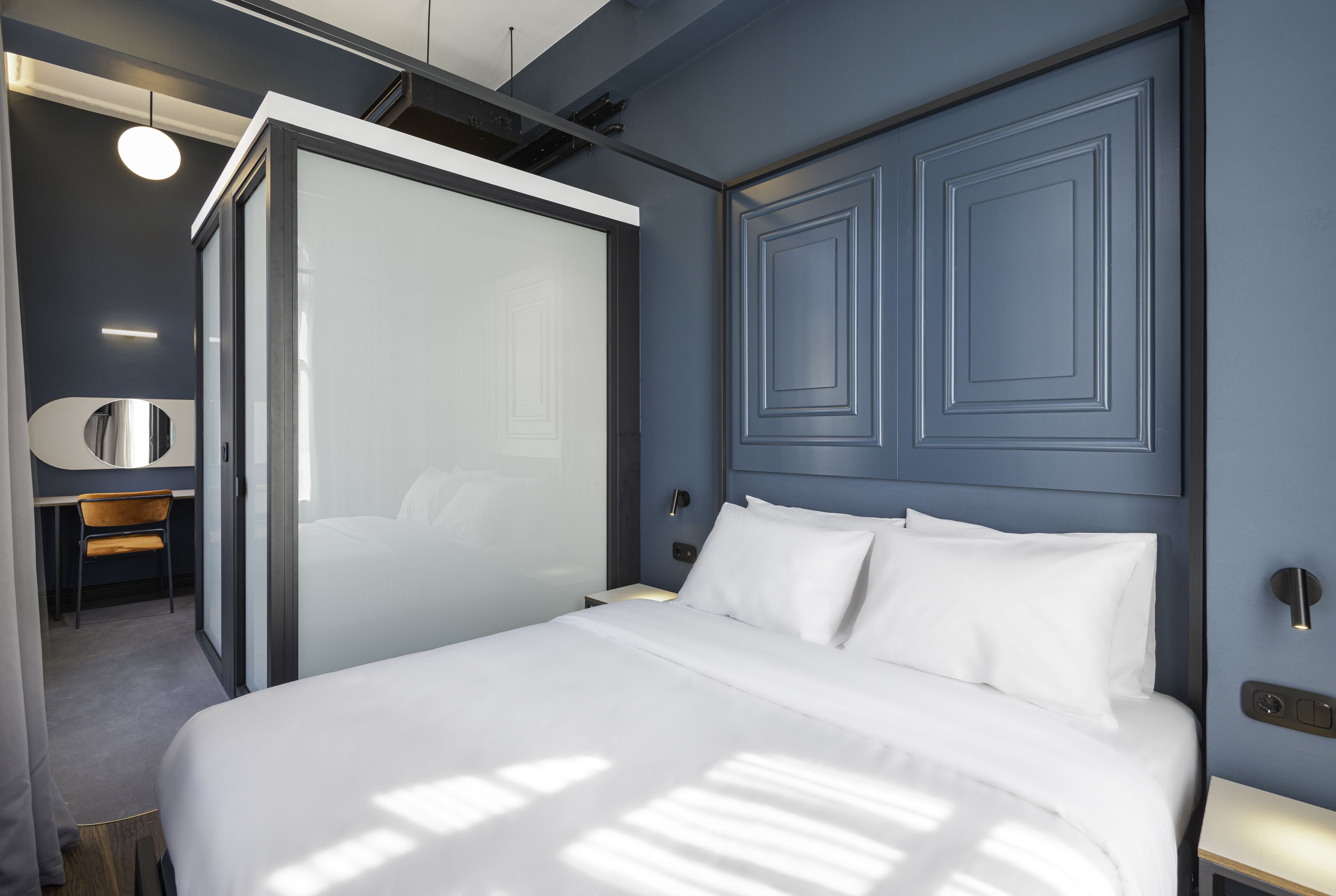 A modern hotel room with a large bed, a desk with a chair, and a walk-in closet.