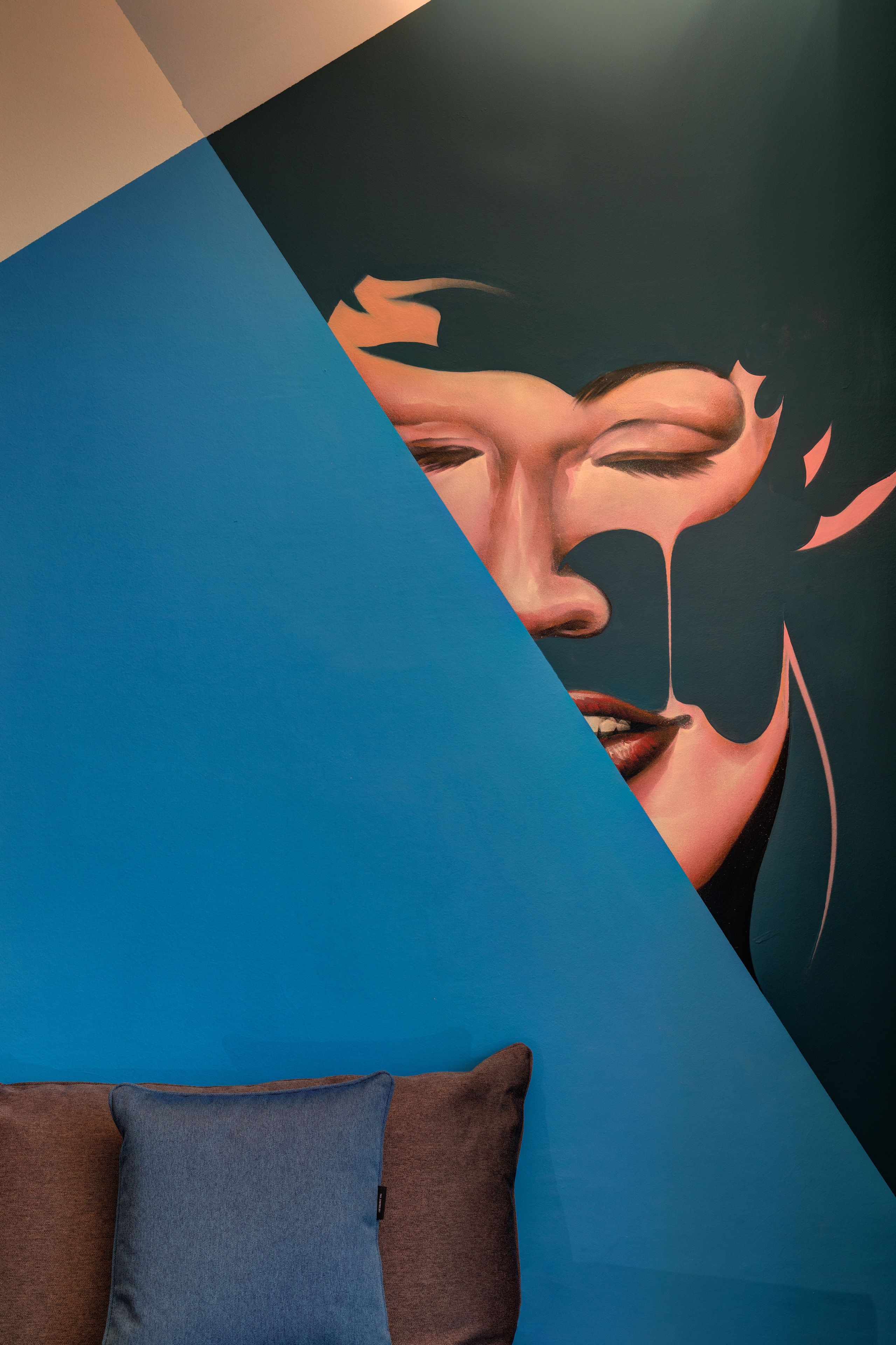 A room with a blue and brown couch, a wall with a geometric design, and a partial view of a window.