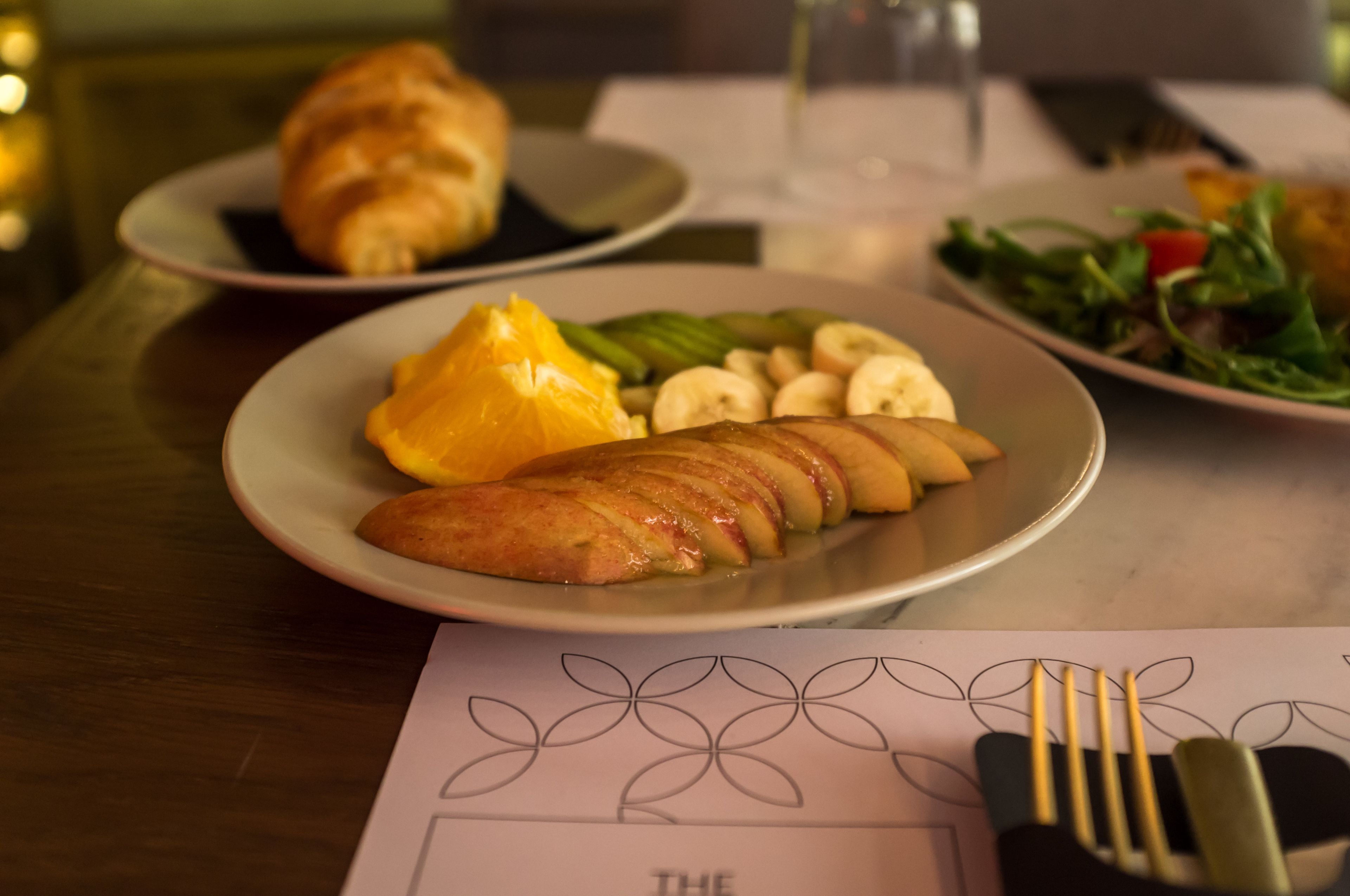 A dining table with plates of food, including a croissant, sliced apples, and a salad.