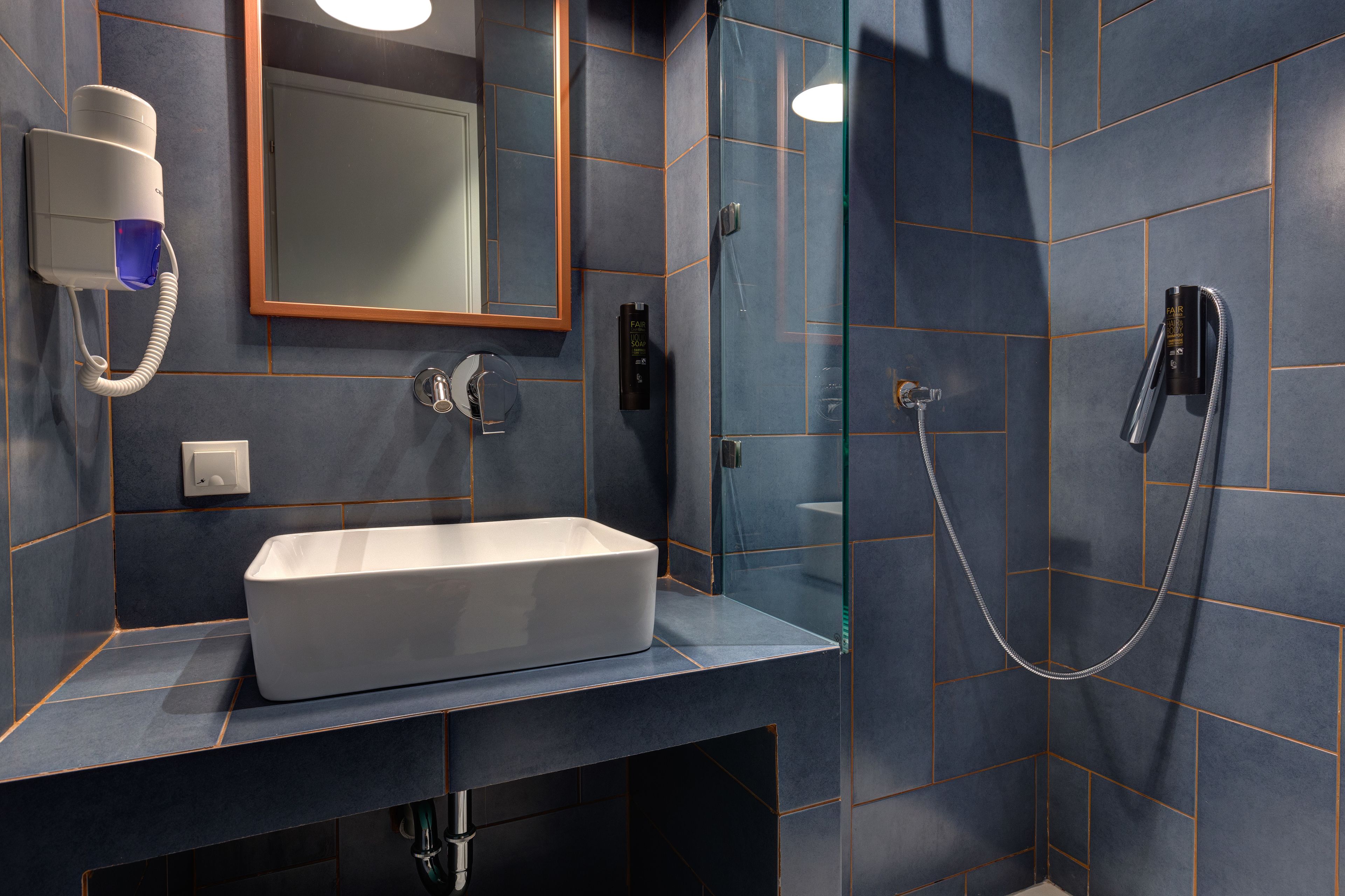 Une salle de bain moderne avec un lavabo rectangulaire, une douchette à main et un sèche-cheveux fixé au mur.