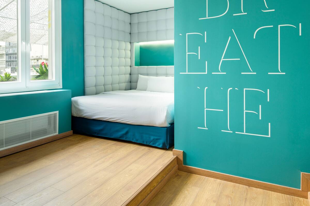 A modern bedroom with a bed, a window, and a wall with 'BREATHE' written on it.