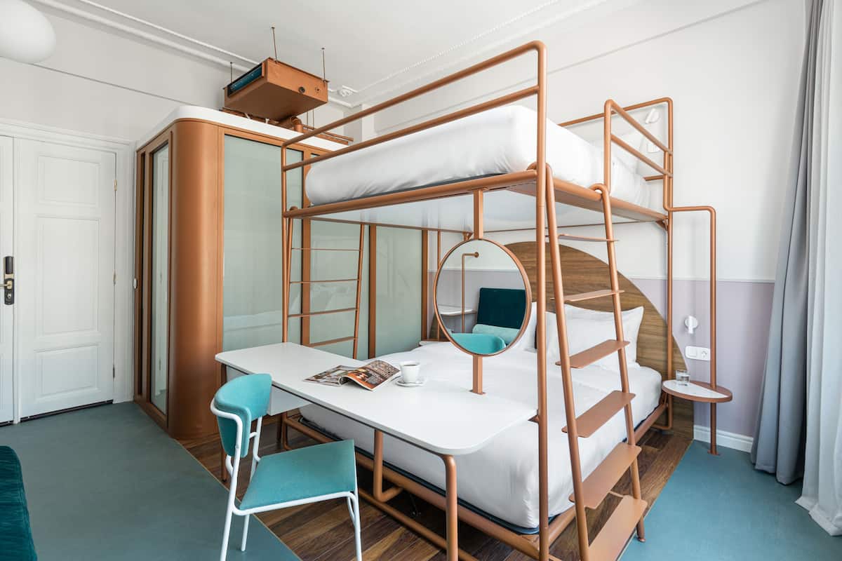 A bunk bed with a desk and chair, a small table, and a mirror.