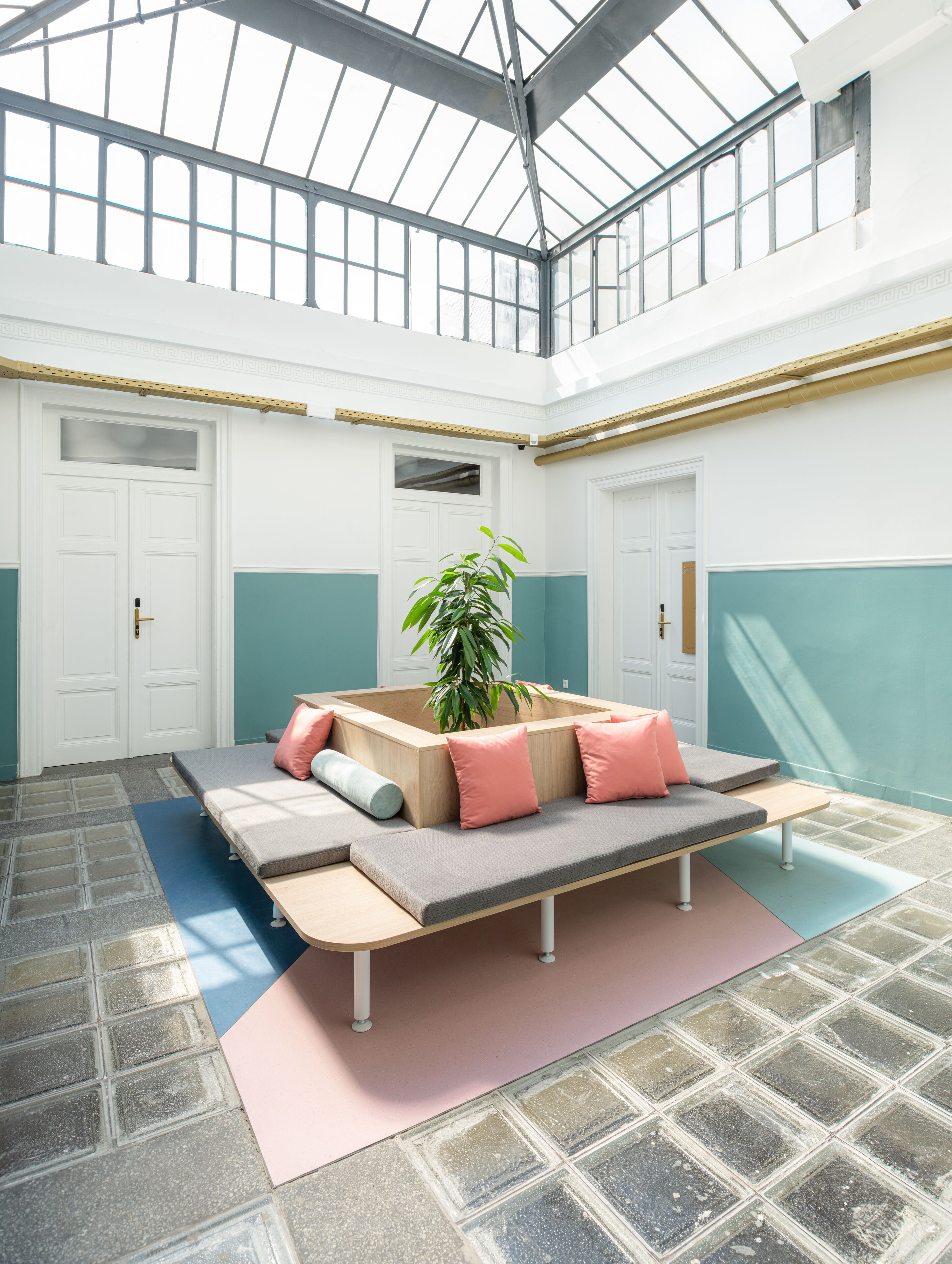 A spacious room with a high ceiling and a skylight, featuring a central seating area with cushions and a potted plant.