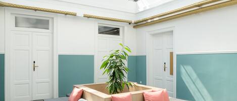 A spacious room with a high ceiling and a skylight, featuring a central seating area with cushions and a potted plant.