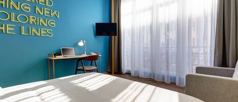 Habitación de hotel con cama, escritorio, ordenador portátil, silla y televisor en la pared.