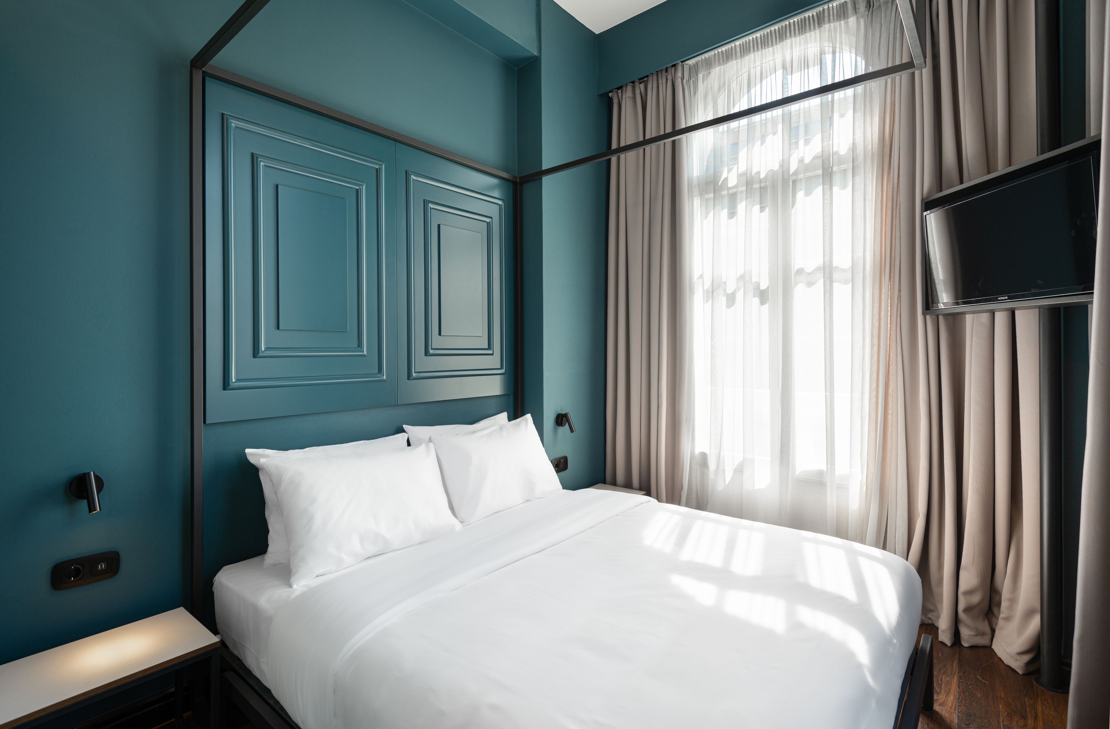 Habitación de hotel moderna con una cama grande, televisor de pantalla plana y ventana con cortinas traslúcidas.