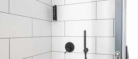A shower with white tiles, a handheld showerhead, and a wall-mounted faucet.