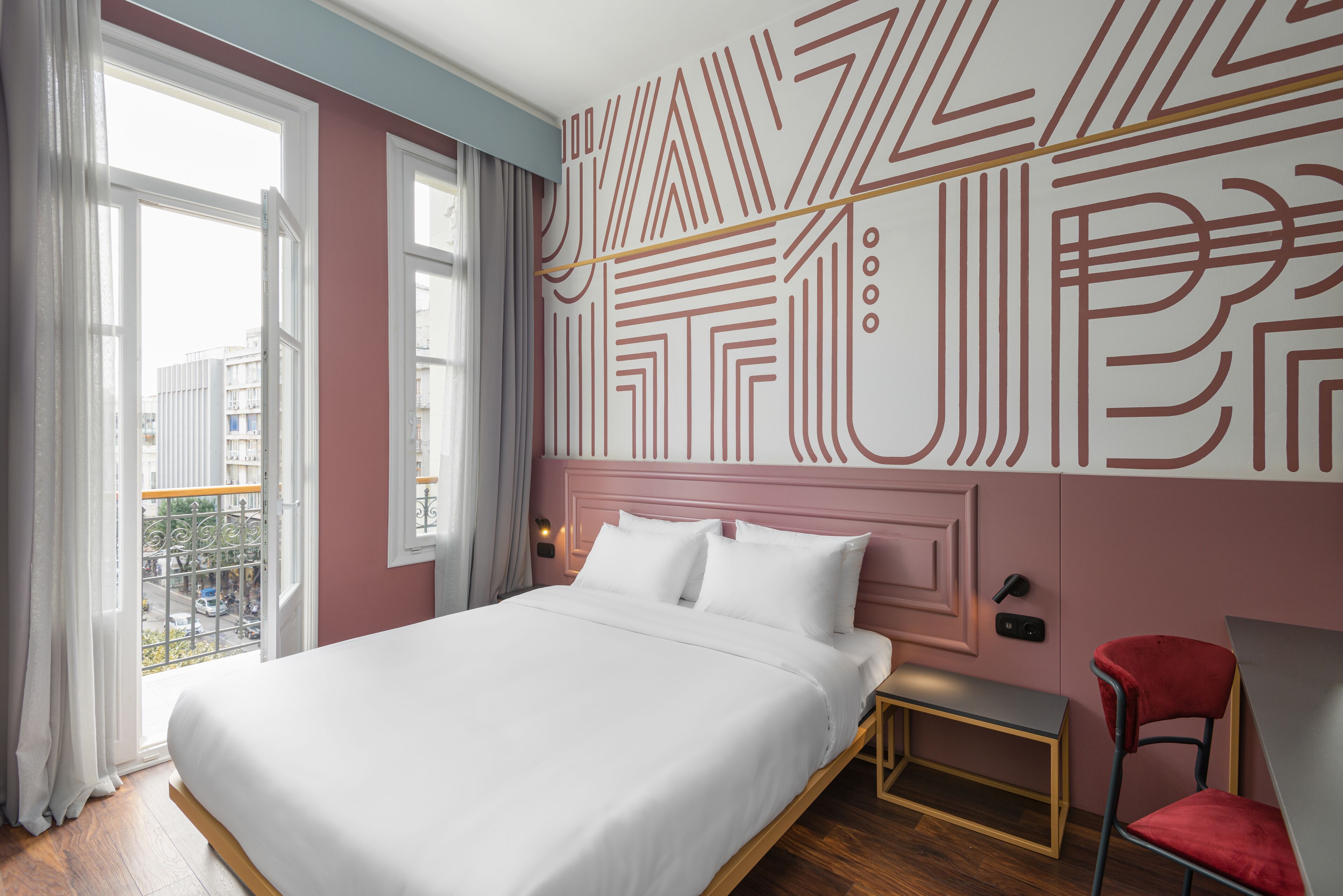 A modern hotel room with a large bed, a bedside table, a chair, and a view of the city through the window.