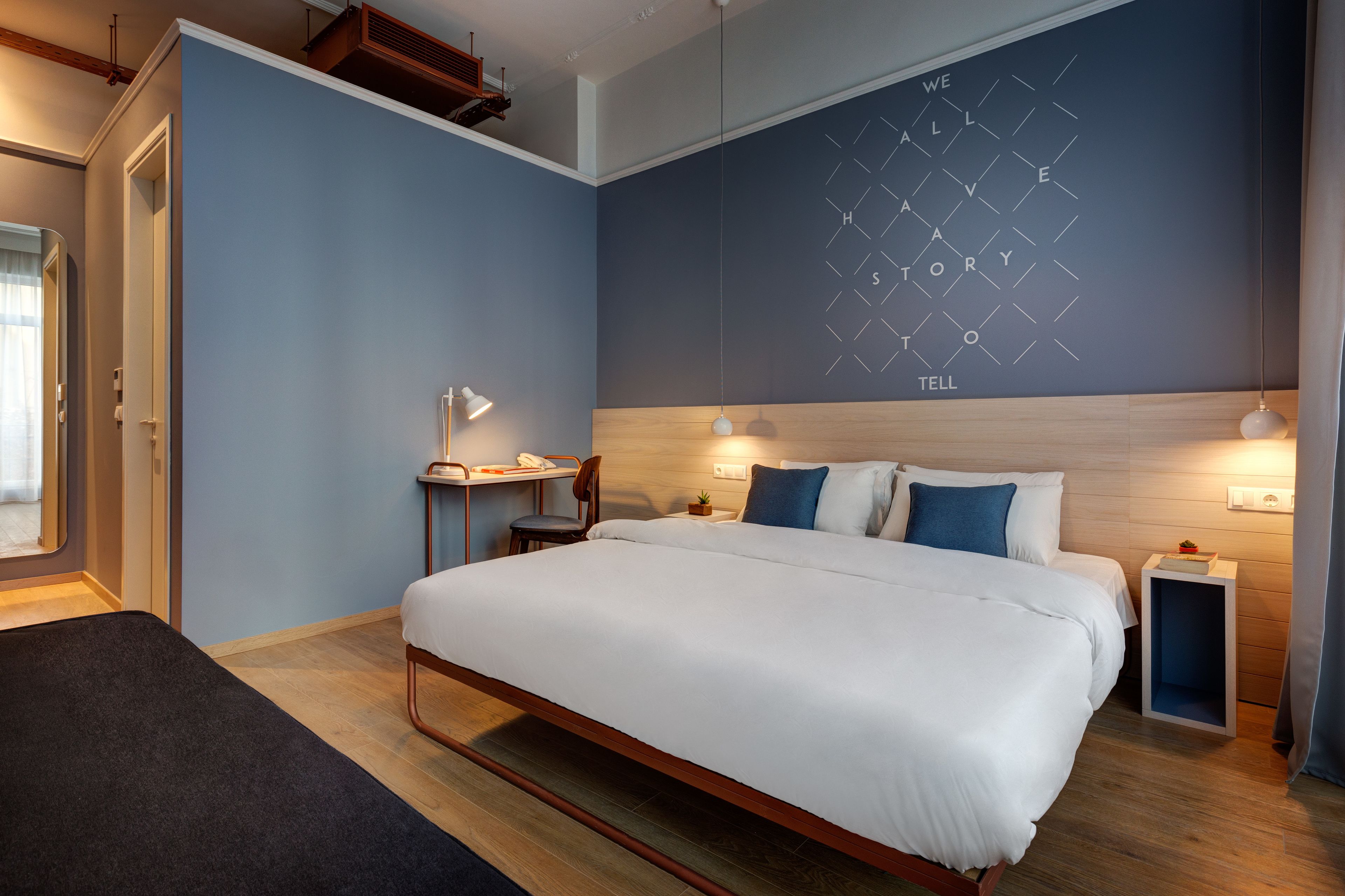 Una habitación de hotel moderna con una cama grande, un escritorio con una silla, una mesita y una pared con diseño geométrico.