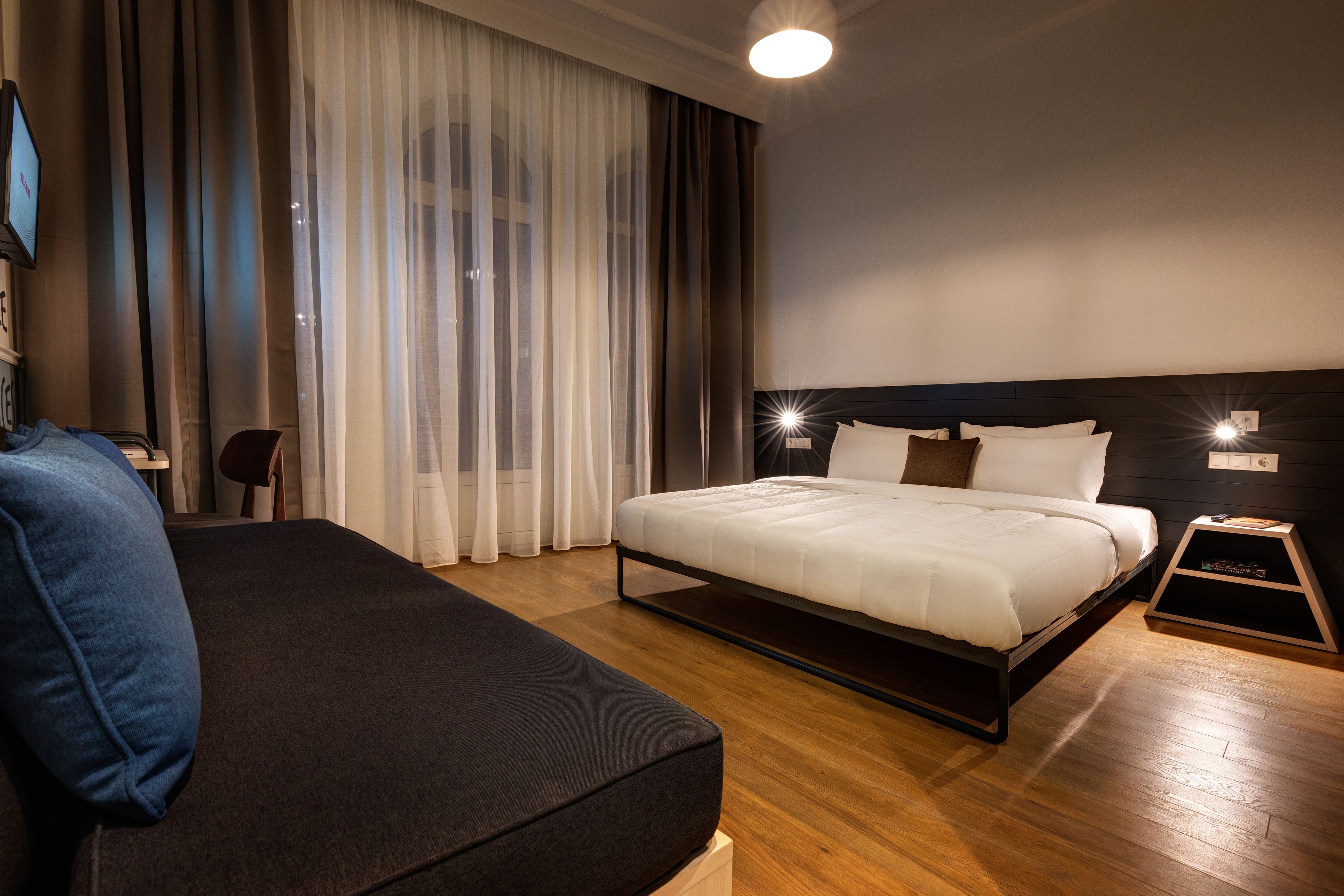 Una habitación de hotel moderna con una cama grande, un sofá y un televisor sobre un soporte.