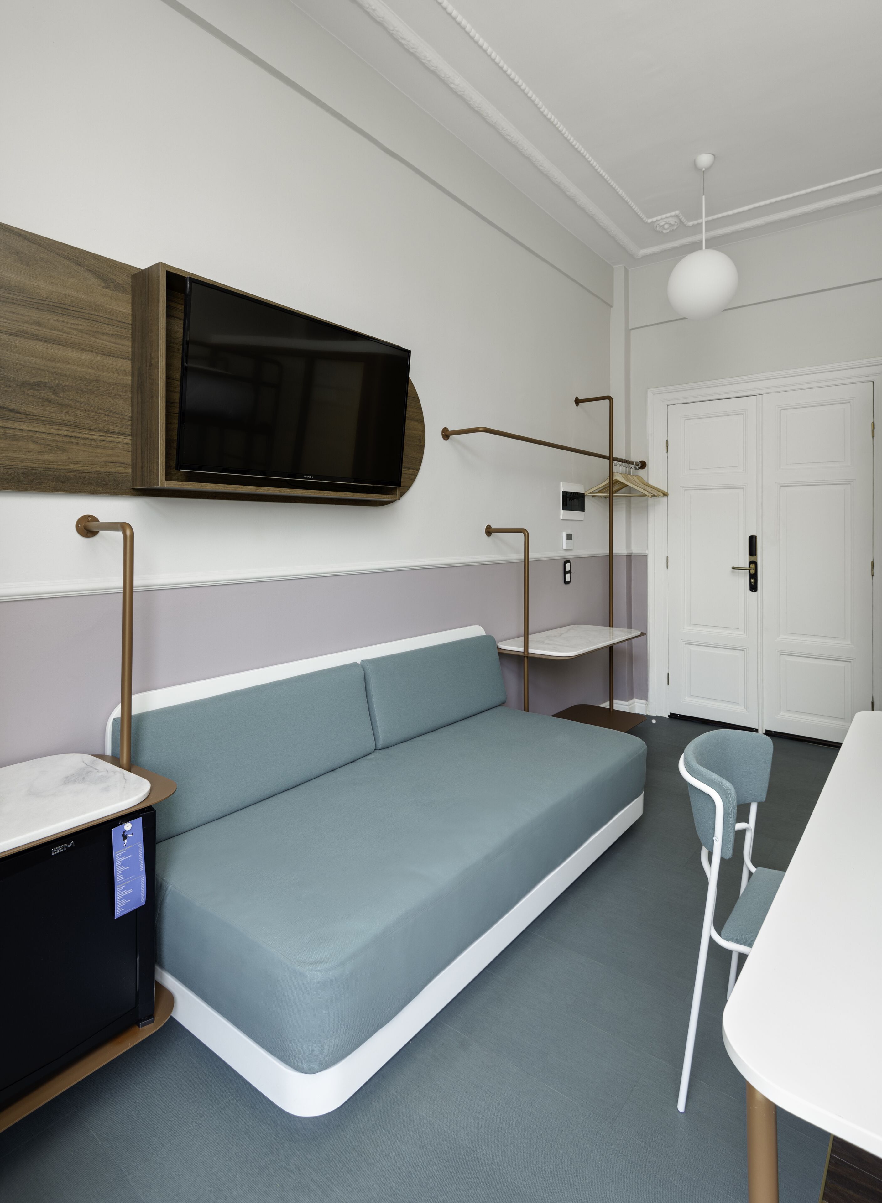 Una habitación moderna con sofá, televisión montada en la pared, mesita de noche, una silla y una puerta.