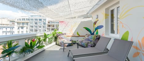 Un balcón con dos sillones, una mesita y un mural de pared colorido.