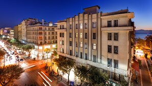 Un edificio de varios pisos con un diseño arquitectónico moderno, que cuenta con una entrada central destacada y una serie de ventanas en la fachada.