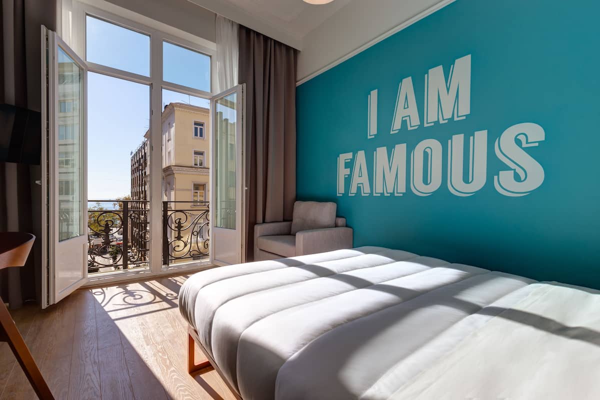 A bedroom with a large bed, a teal accent wall, and a balcony with a city view.