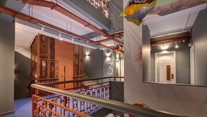 Un interior de varios niveles con una escalera que presenta barandales metálicos ornamentados y tuberías expuestas en el techo.