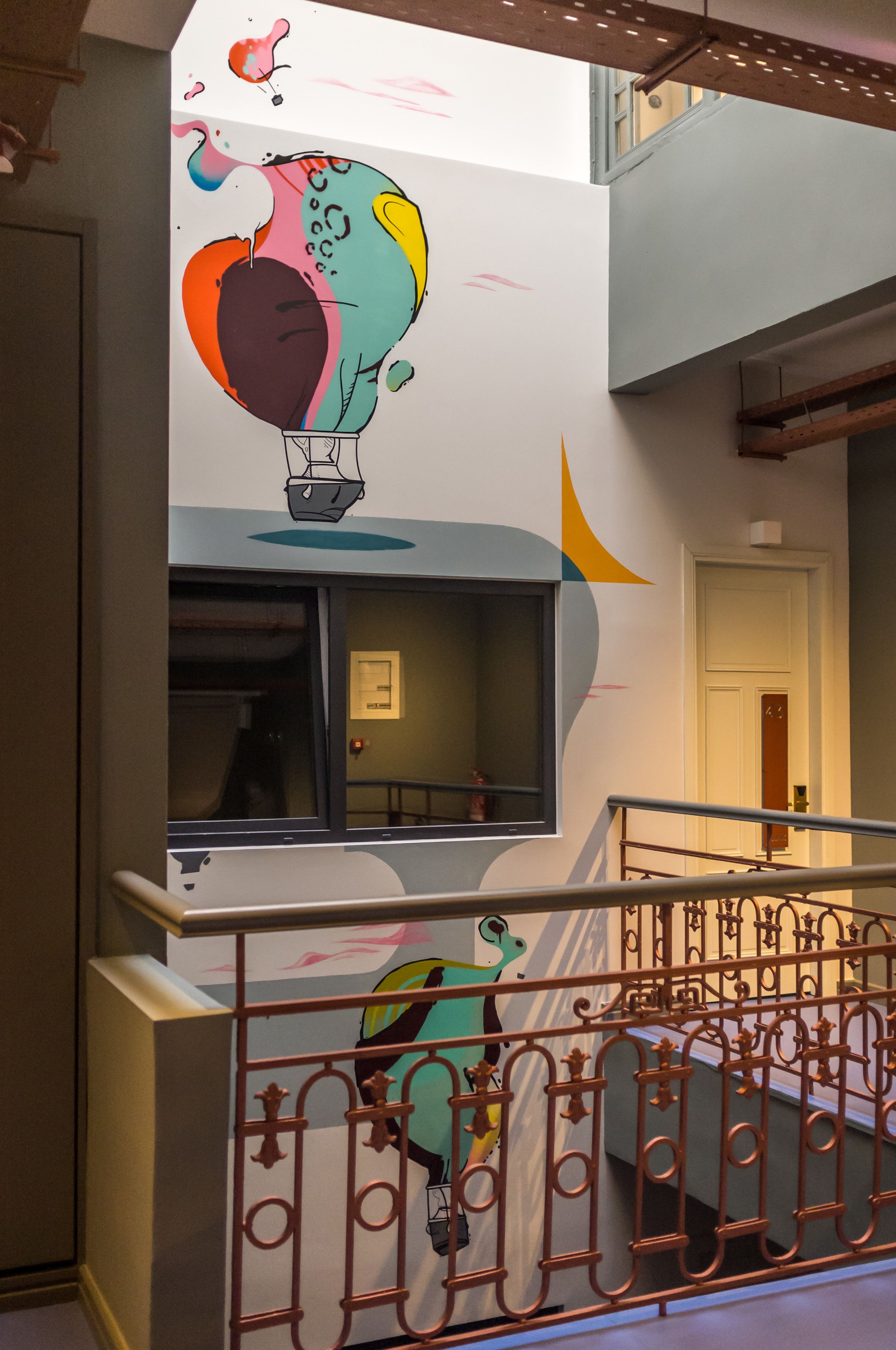 A staircase with a colorful mural, a metal railing, and a door in the background.