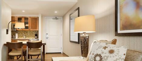 A hotel room with a dining area, a sofa with patterned cushions, a lamp, and a framed picture on the wall.