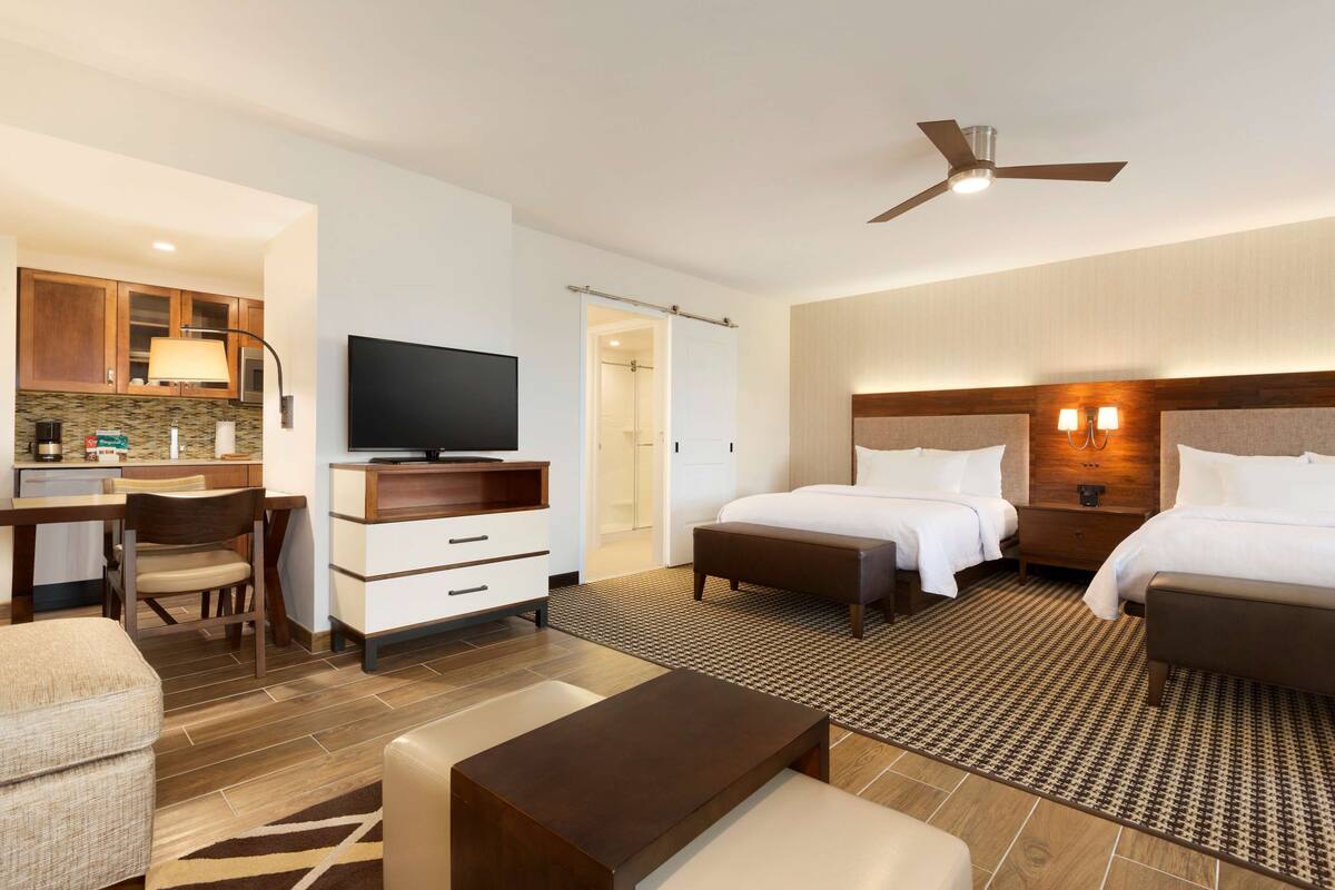 A hotel room with a bed, bedside tables, a TV, a desk with a chair, and a kitchenette.