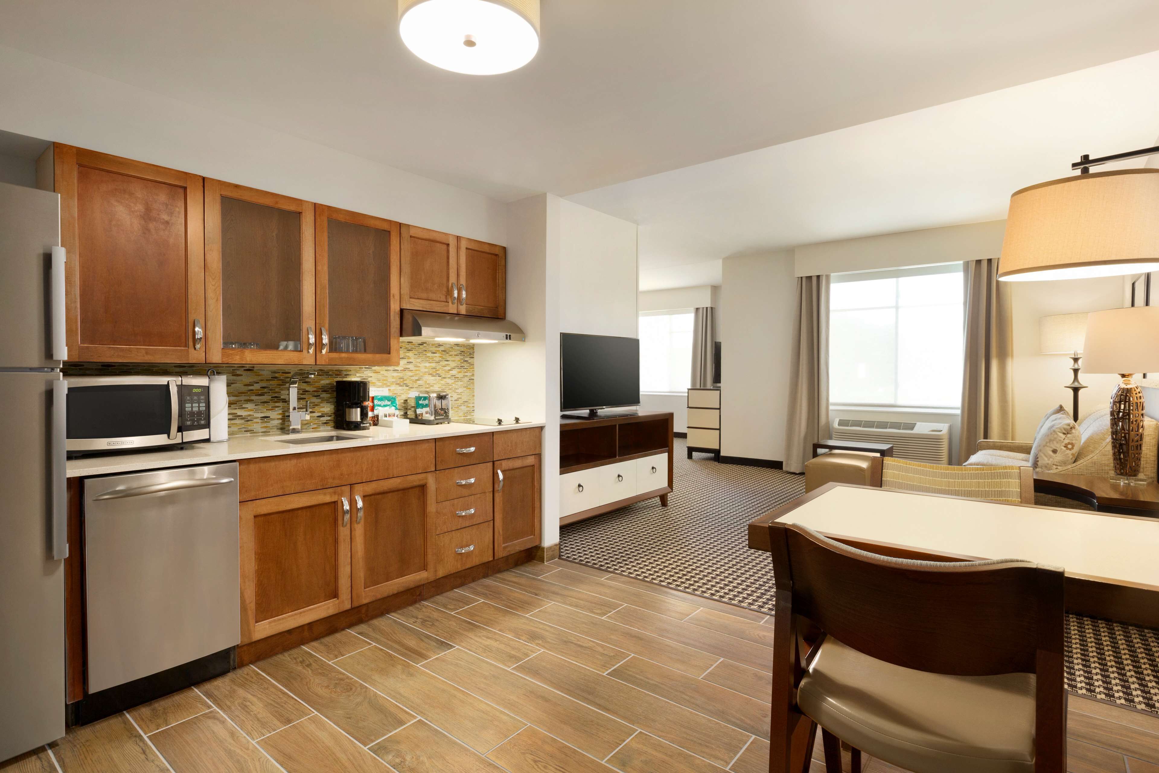 A modern kitchen with wooden cabinets, a microwave, and a dishwasher. There is a dining area with a table and chairs.