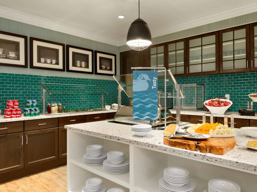 A modern kitchen with a teal backsplash, wooden cabinets, and a central island with food items and plates.
