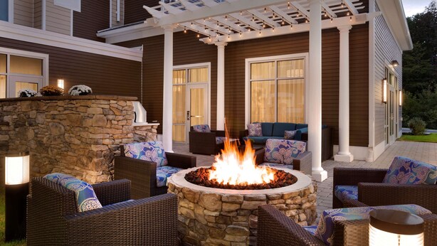 An outdoor patio with a stone fire pit surrounded by wicker furniture and a pergola with string lights. - Homewood Suites by Hilton Augusta (Augusta)