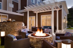 An outdoor patio with a stone fire pit surrounded by wicker furniture and a pergola with string lights. - Homewood Suites by Hilton Augusta (Augusta)
