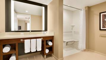 A modern bathroom with a large mirror, wooden vanity, multiple towels, a shower area, and a framed picture on the wall.