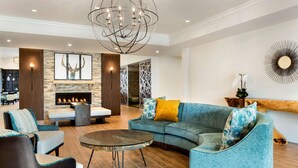 A modern living room with a curved blue sofa, a round coffee table, and a fireplace. - Homewood Suites by Hilton Augusta (Augusta)